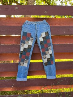 a pair of blue jeans with patchwork on them hanging from a wooden fence outside