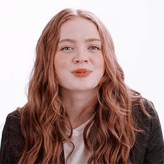 a woman with long red hair wearing a black jacket and white t - shirt is looking at the camera