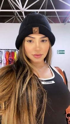 a woman with long hair wearing a beanie and looking at the camera while standing in a clothing store