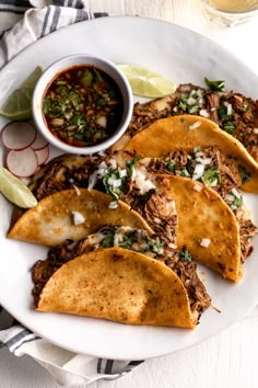 some tacos are on a white plate with salsa and lime wedges next to it