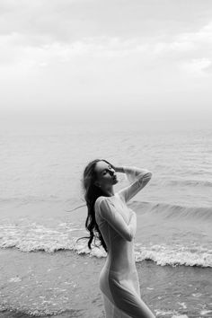 a woman standing on top of a beach next to the ocean holding her hair up