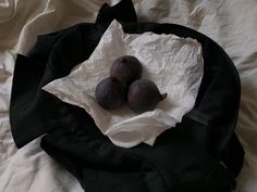 three plums sitting on top of a black cloth in a white paper wrapper