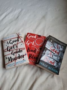 three books laying on top of a bed next to each other in front of a white sheet