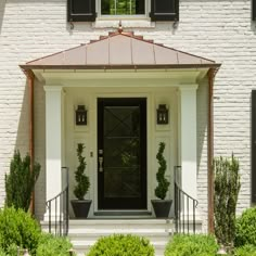 a white house with black shutters and two potted plants on the front porch