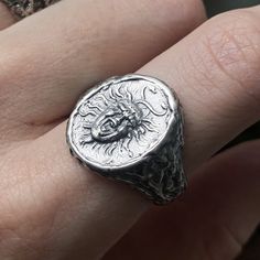 a person's hand holding a silver ring with a scorpion design on the middle