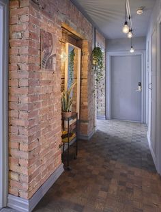 an empty hallway with brick walls and wood flooring on the other side is a potted plant