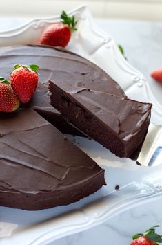 there is a chocolate cake with two slices taken out and strawberries on the plate