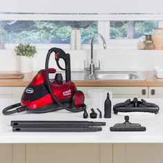 a red and black vacuum is sitting on the kitchen counter next to other cleaning supplies