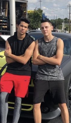 two young men standing next to a sports car