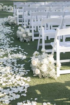 the aisle is lined with white chairs and petals on the grass, as well as flowers