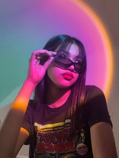 a woman with dark hair and sunglasses is posing in front of a neon circle wall