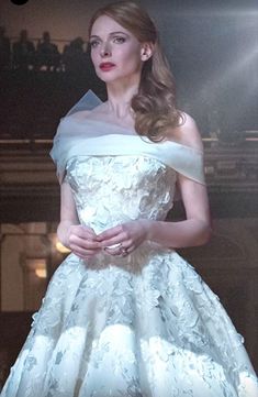 a woman in a white dress standing on a stage with her hands clasped to her chest