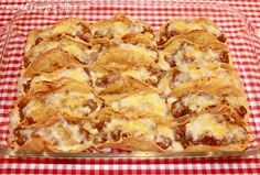 a glass casserole dish filled with cheese and meat nachos on a checkered tablecloth