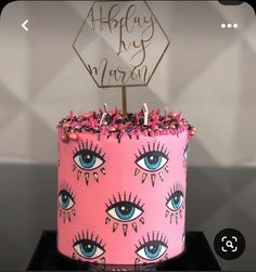 a pink cake with blue eyes on it and a happy birthday sign in the middle