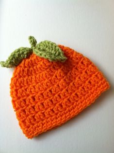 an orange crocheted hat with a green leaf on it's top, sitting on a white surface