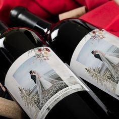 two bottles of wine sitting next to each other on top of a wooden table covered in red cloths