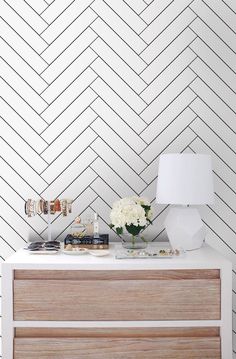 a dresser with flowers and candles on it in front of a white herringbone wall