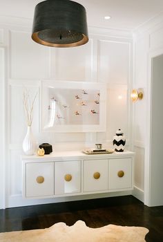 a room with white cabinets and gold handles on the doors, an area rug and a black lamp hanging from the ceiling