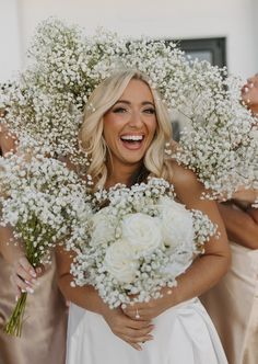 a woman in a wedding dress is holding flowers and smiling at the camera while another woman holds her bouquet behind her back