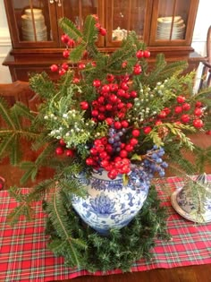 a blue and white vase filled with red berries on top of a wooden tablecloth