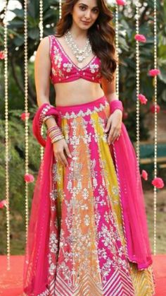 a woman in a pink and yellow lehenga with beads hanging from the ceiling