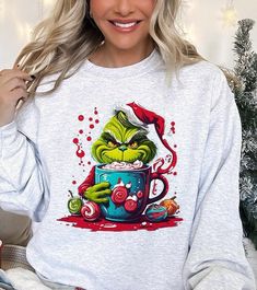 Indulge in the festive fun with this 'Giggling Grinch' unisex fleece sweatshirt! This merry piece is perfect for celebrating Grinchmas, showcasing a vibrant graphic of the iconic character enjoying a hot holiday treat. Made from a snug 50% cotton and 50% polyester mix, it promises warmth and softness for the chilly holiday season. This unisex sweatshirt, originating from Nicaragua, provides a comfortable fit for all, making it an excellent choice for holiday gifting or for bringing some playful Diy Grinch Shirt, Grinch Christmas Sweater, Diy Grinch, Snap Jewelry Charms, Grinch Shirt, Essential Oil Accessories, Sweatshirt Graphic, Oversized Graphic Tee, Plus Swimwear