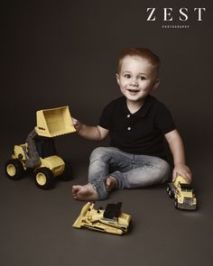 a young boy sitting on the ground with toys in front of him and smiling at the camera