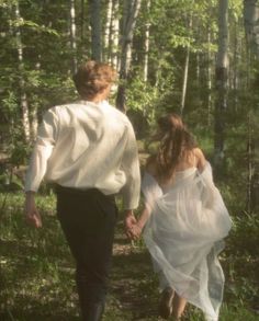 a man and woman walking through the woods holding hands