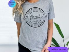 a woman wearing a gray shirt with the words 5th grade co in black on it