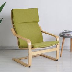 a green chair next to a small table with a plant on it and a magazine