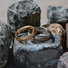 two gold wedding rings sitting on top of rock next to another ring in front of them