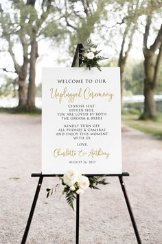 a welcome sign with flowers and greenery is displayed on an easel in front of trees