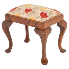 a small wooden stool with a red and yellow flower pattern on the seat padding