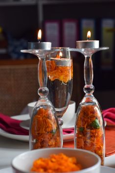 two candles are sitting on top of some glass vases with food in them next to plates and napkins