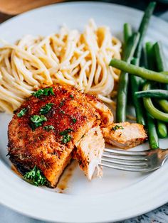 a white plate topped with pasta and meat next to green beans on a wooden table