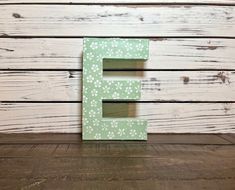 the letter e is made out of wood and has white flowers on green painted letters