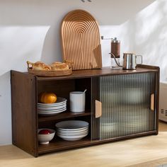 a wooden cabinet with plates and bowls on it next to a toaster, bread basket and other kitchen items