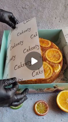 someone in black gloves is holding up a box with oranges and cake inside it