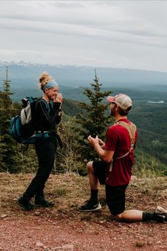 two people sitting on top of a mountain with backpacks and talking to each other