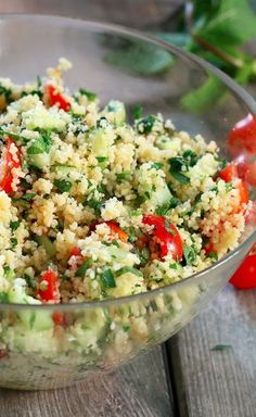 a glass bowl filled with couscous and veggies on top of a wooden table