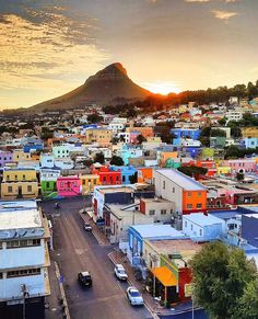 the sun is setting over a city with colorful buildings and mountains in the back ground