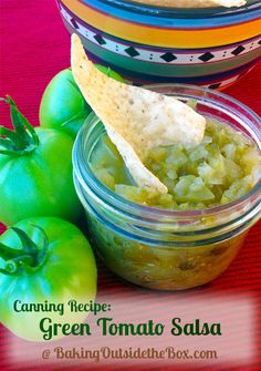 green tomato salsa with tortilla chips in a glass jar and tomatoes on the side