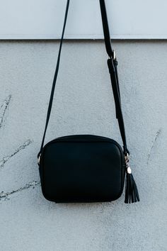 This camera-style crossbody has an accent tassel on the zipper pull. It has one zippered pocket and one open pocket inside the bag, and the crossbody strap is adjustable. It's a perfect size for travel! Dimensions: 6.5" tall by 8.5" wide 3.25" base Black Travel Shoulder Bag With Tassels, Travel Crossbody Shoulder Bag With Tassels, Everyday Tassels Crossbody Shoulder Bag, Black Tassel Crossbody Bag, Black Shoulder Bag With Tassels For Everyday Use, Faux Leather Handbag, Zipper Pulls, Black Cross Body Bag, Black Faux Leather