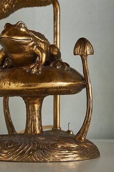 a gold frog sitting on top of a golden chair with two mushrooms in front of it