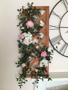 a clock mounted to the side of a wall next to a flower arrangement on top of a wooden frame