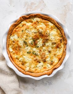 an overhead view of a quiche in a white pie dish on a marble surface