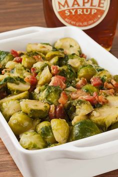 brussel sprouts and bacon in a white dish next to a bottle of maple syrup