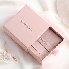 the pink box is next to some earrings on a white cloth with flowers in it