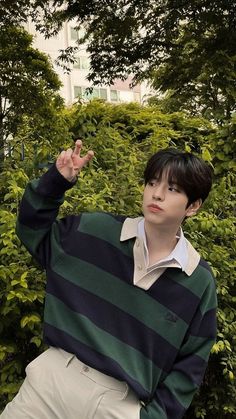 a young man standing in front of some bushes wearing a green and black striped sweater