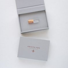 an open box with a ring in it on top of a white table next to a card